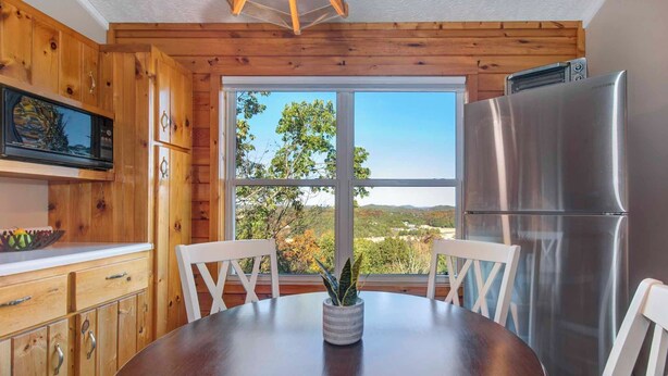 A wooden kitchen with a stainless steel refrigerator, a dining table with chairs, and a large window offering a view of the outdoors. - Near Douglas Lake: Mountain Jewel Haven w/ Views (Sevierville)