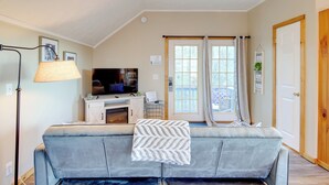 A living room with a grey sofa, a television, a fireplace, and a large window with curtains. - Near Douglas Lake: Mountain Jewel Haven w/ Views (Sevierville)