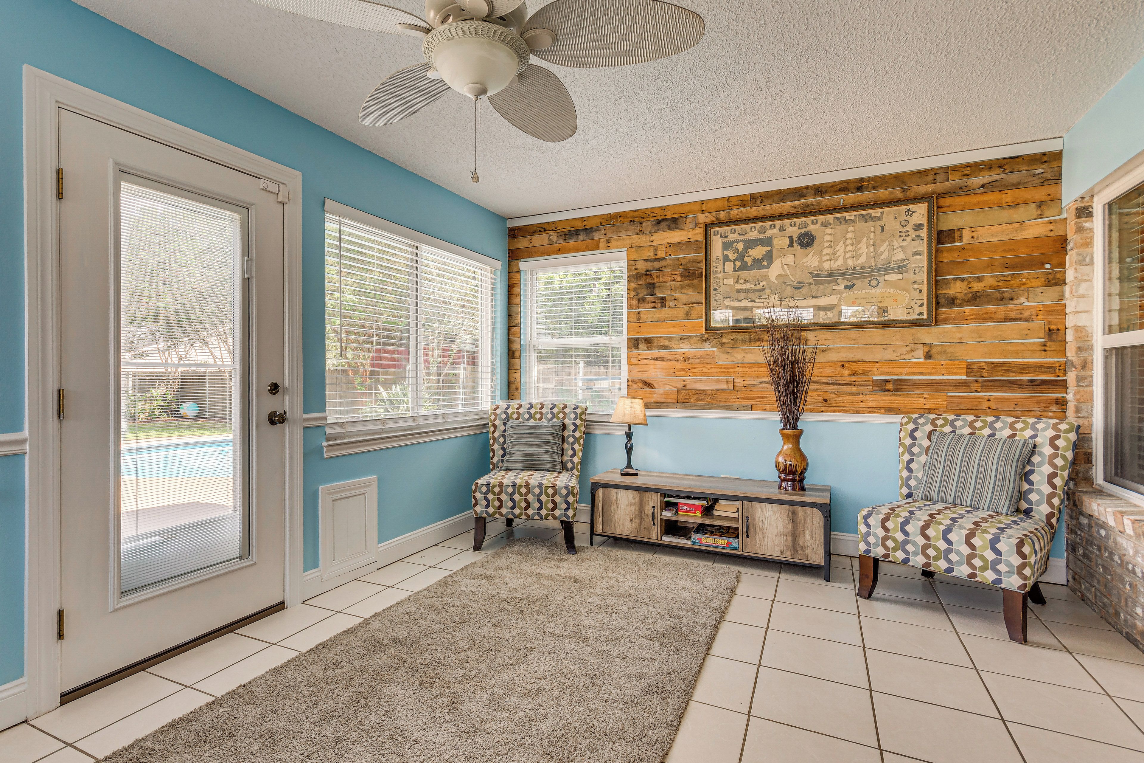A room with a blue wall, a wooden accent wall, a ceiling fan, two patterned armchairs, a side table with a lamp, and a framed picture.