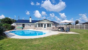 A backyard with a swimming pool, a covered patio area, and a fenced yard.