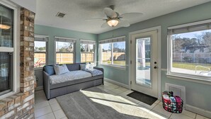 A room with a grey sofa, a ceiling fan, and a view of a backyard through large windows.