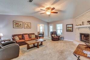A living room with a fireplace, a ceiling fan, and a dining area with a table and chairs.