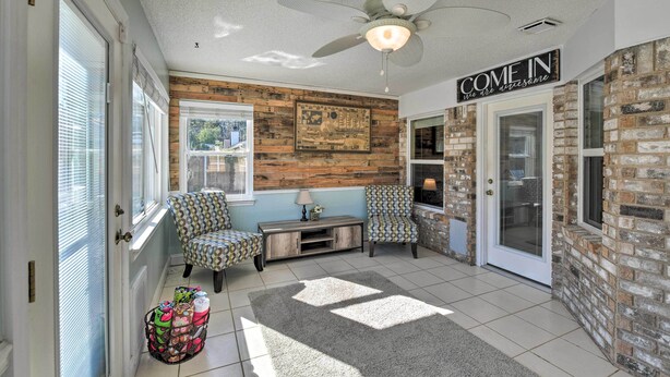 A spacious entryway with a ceiling fan, a 'COME IN' sign, two patterned armchairs, a small console table, and a decorative rug.