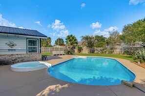 A swimming pool with a hot tub, a patio with outdoor furniture, and a house with a metal roof. - Welcoming Pensacola Home w/ Spacious Yard! (Pensacola)