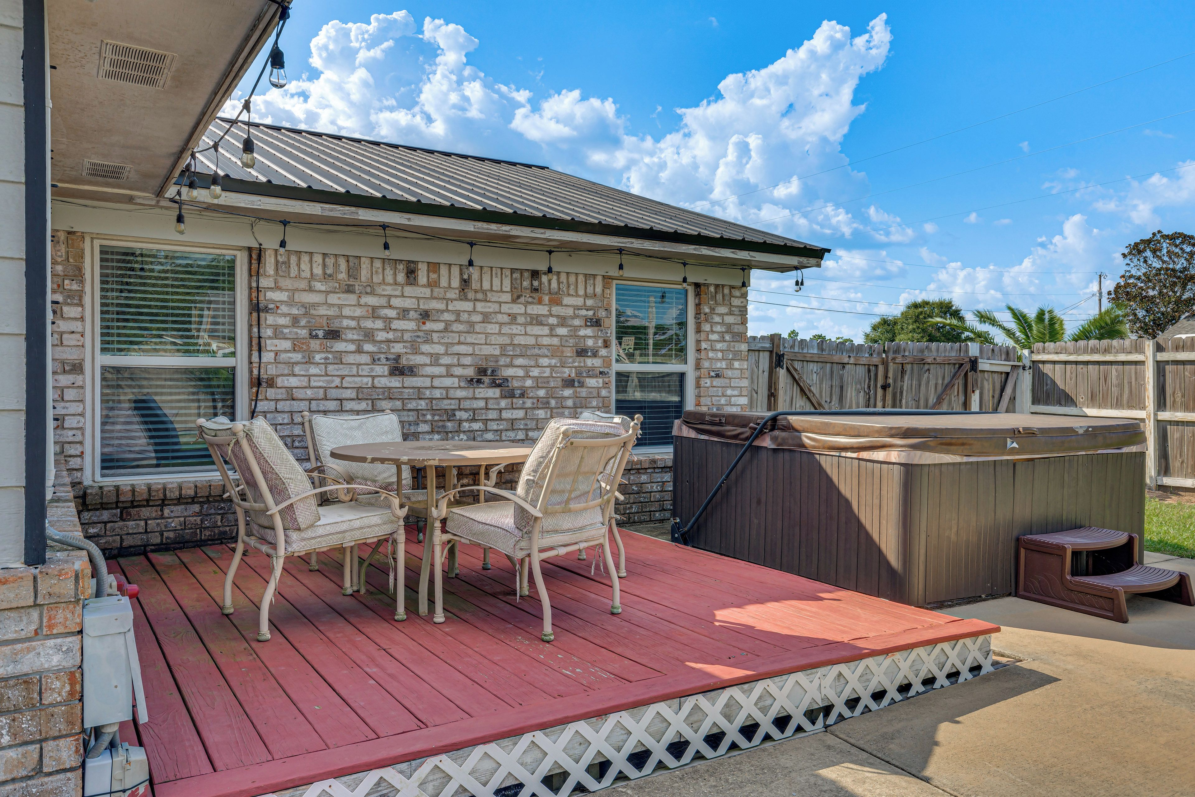 Un patio cubierto con muro de ladrillo, terraza de madera, jacuzzi y mobiliario exterior.