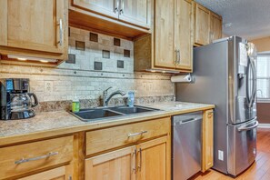 A kitchen with wooden cabinets, a stainless steel refrigerator, a coffee maker, and a dishwasher. - Welcoming Pensacola Home w/ Spacious Yard! (Pensacola)
