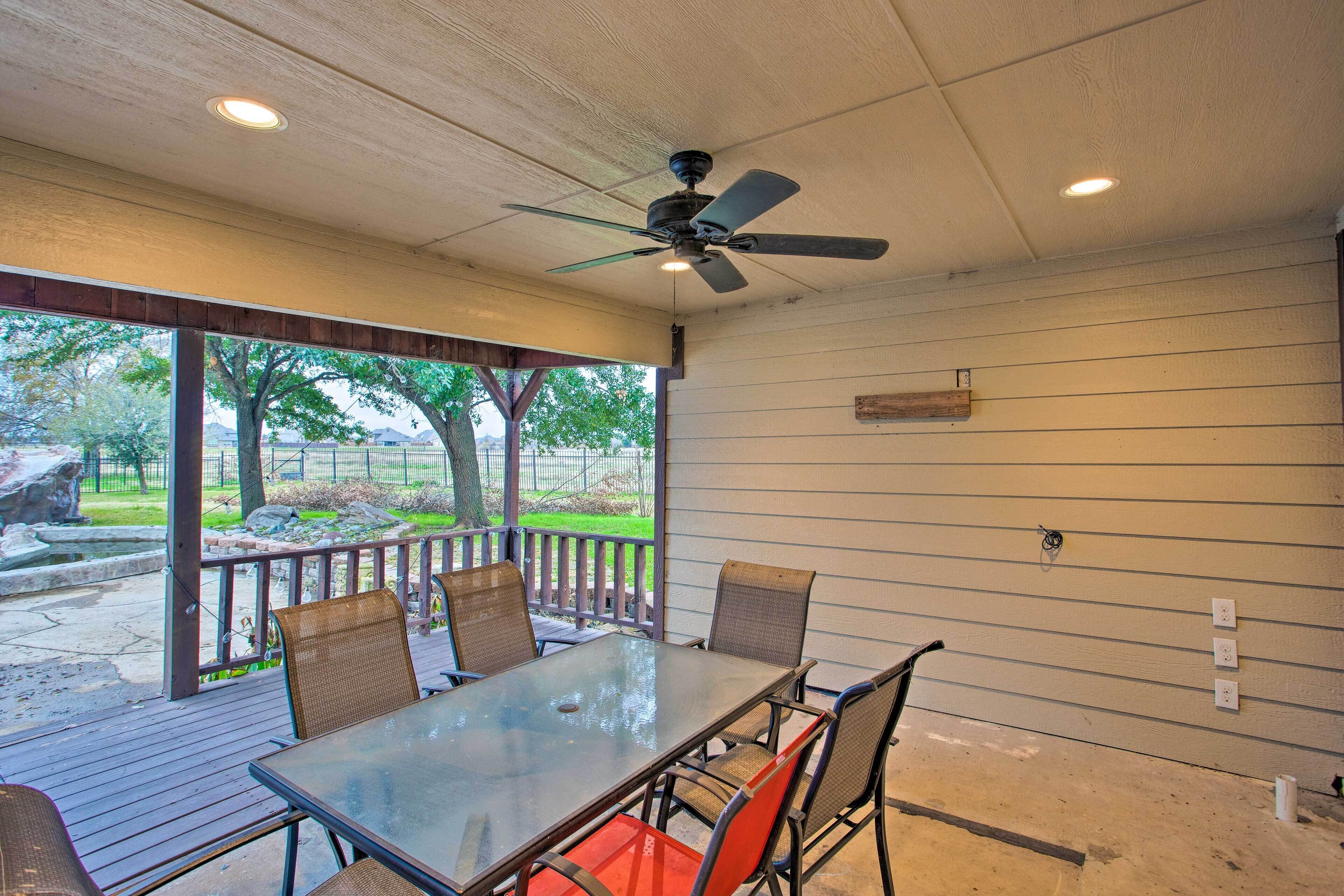 An outdoor patio with a table and chairs, a ceiling fan, and a view of the outdoors.