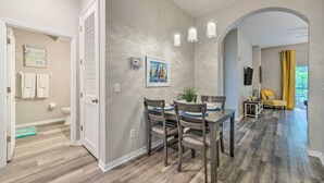 A dining area with a wooden table and chairs, a painting on the wall, and a view into the adjacent living room. - Resort Condo w/ Patio + Pool Access in Davenport! (Davenport)