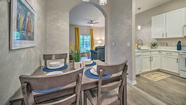 A dining area with a wooden table and chairs, a painting on the wall, and a kitchen in the background. - Resort Condo w/ Patio + Pool Access in Davenport! (Davenport)