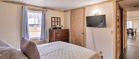 Un dormitorio con cama, cómoda, televisor y puerta corredera que da a otra habitación.