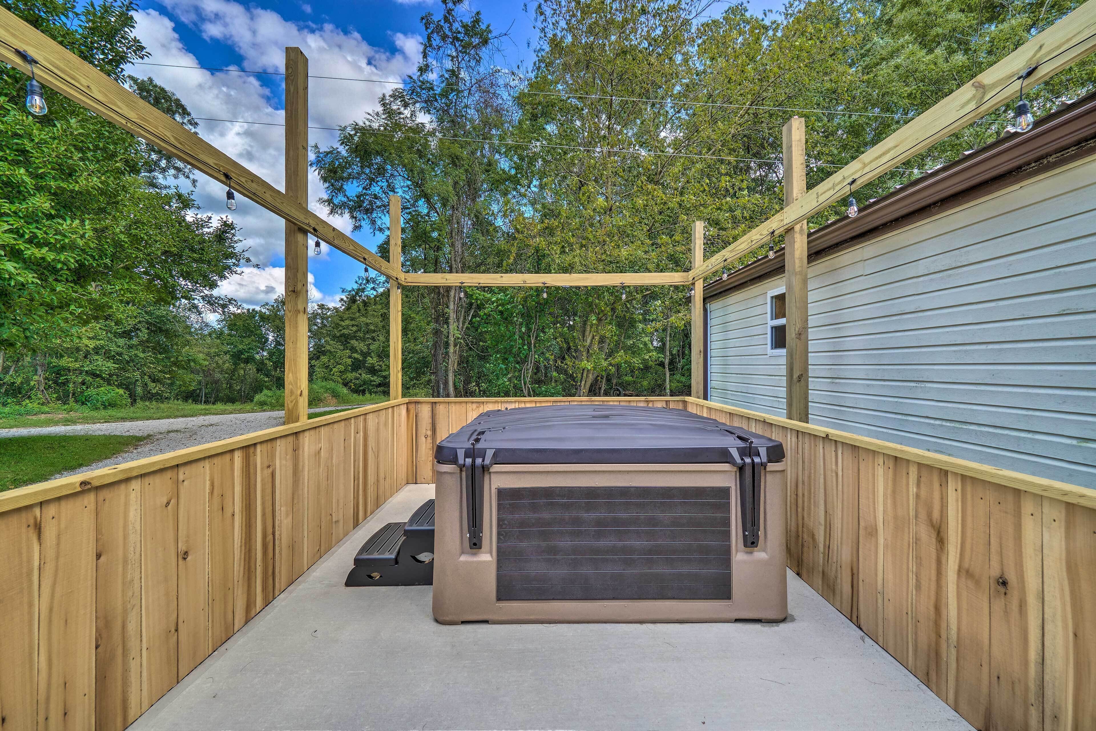 Una terraza de madera con un jacuzzi, rodeada por una cerca de metal y árboles.
