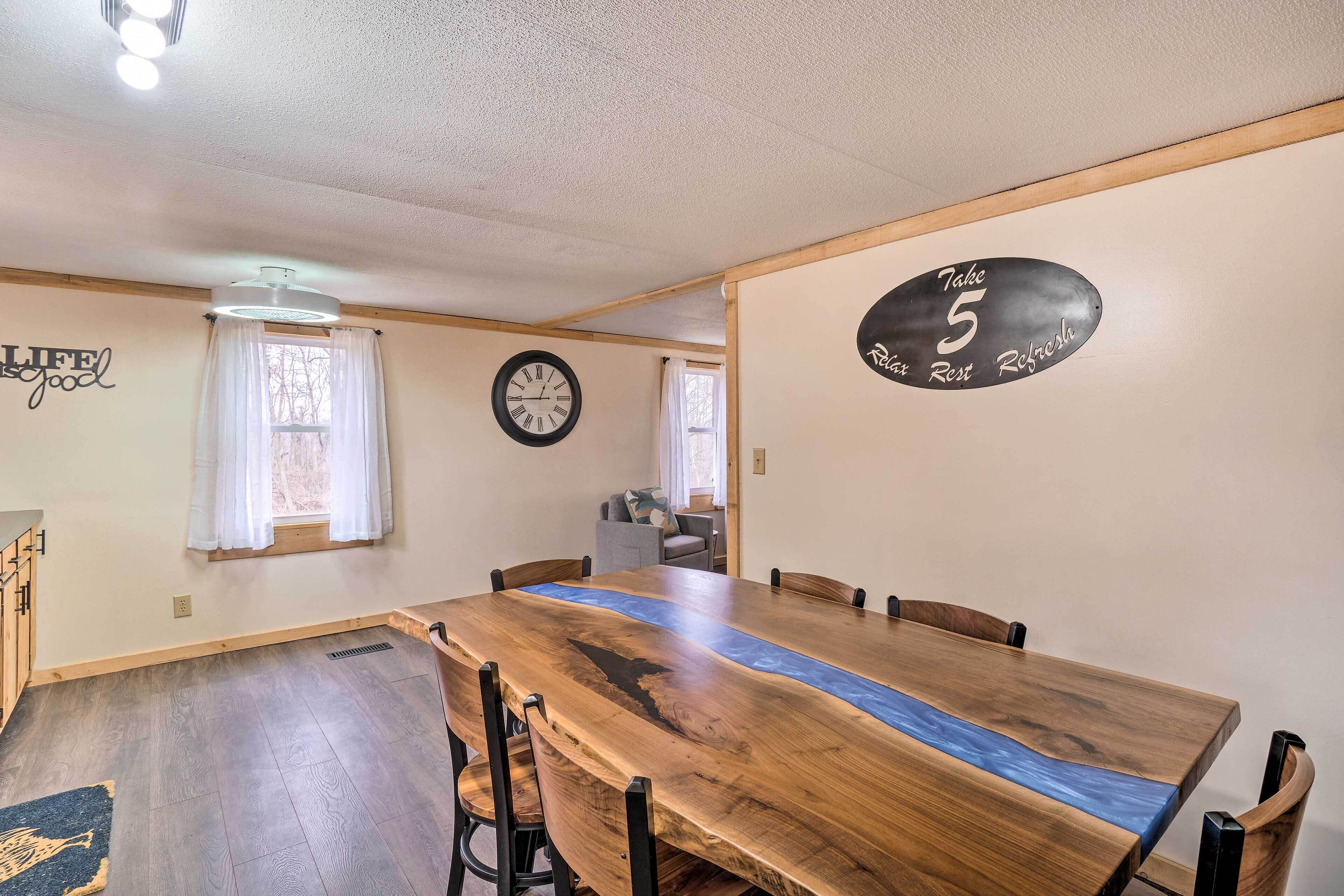 A dining area with a large wooden table, chairs, a clock, and a sign on the wall.