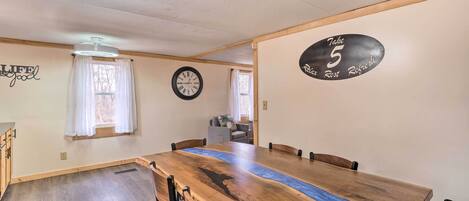 A dining area with a large wooden table, chairs, a clock, and a sign on the wall.