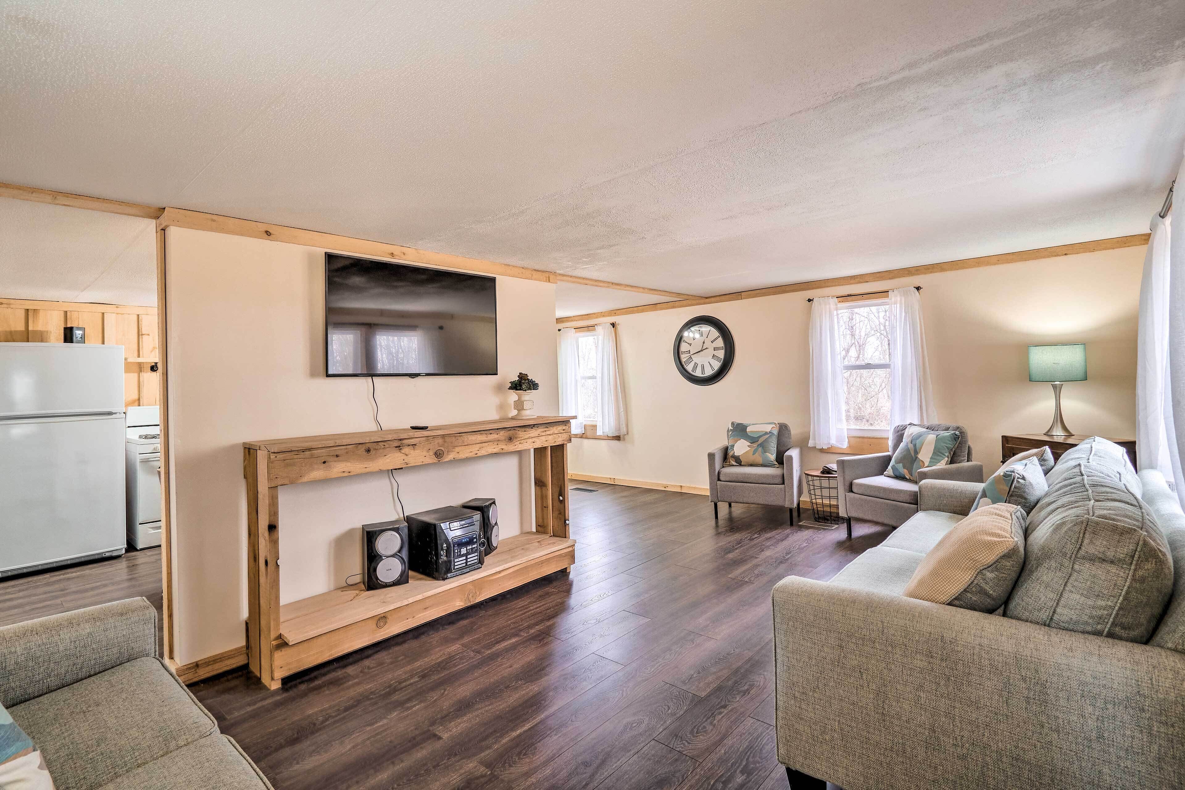 Un salon comprenant un meuble TV en bois, un canapé, une table à manger et un coin cuisine avec un réfrigérateur.