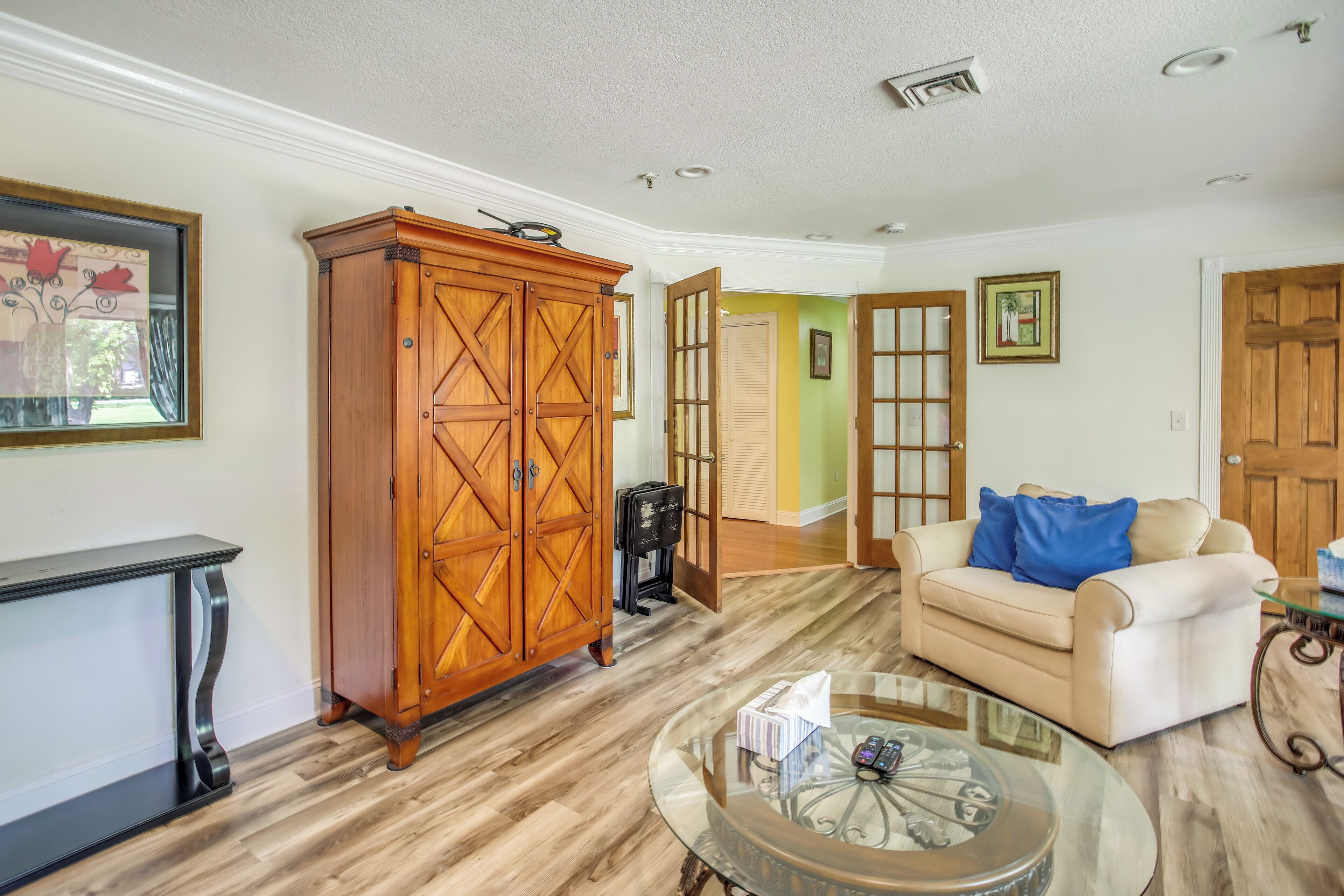 A living room with a wooden cabinet, a glass coffee table, and a beige sofa with blue cushions.