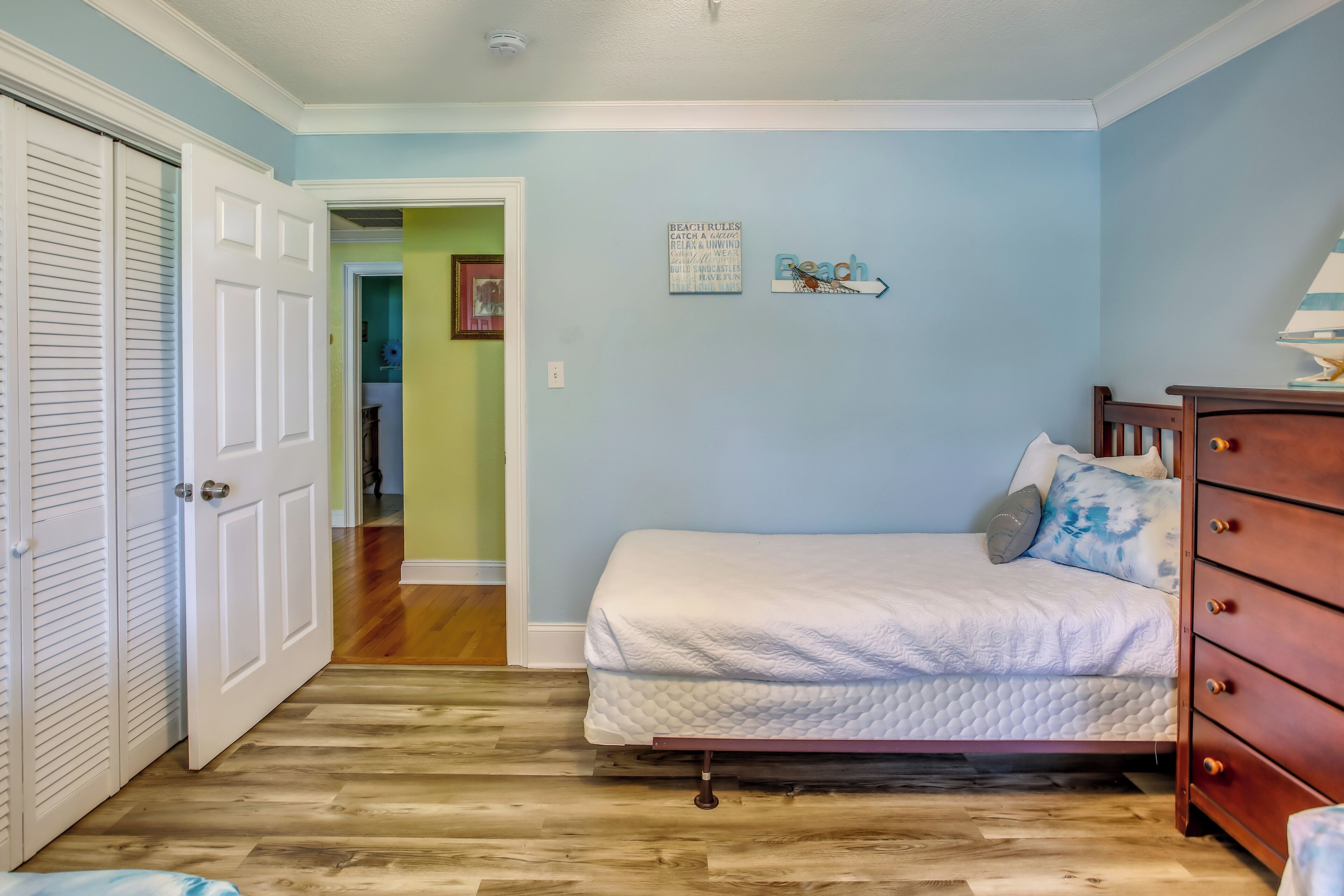 Une chambre à coucher avec un lit, un plancher en bois, une commode et une porte.