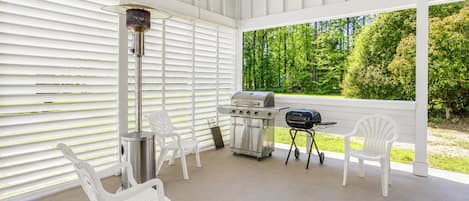 A covered patio with white chairs, a grill, and a portable heater.