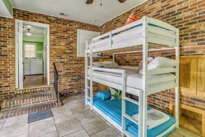 Habitación con literas, pared de ladrillo, puerta que da a un área de lavandería y un armario de madera.