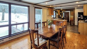 A spacious dining area with a wooden table and chairs, a kitchen in the background, and large windows offering a view of a snowy outdoor area. - Burlington Flats House < 13 Mi to Cooperstown! (Burlington Flats)