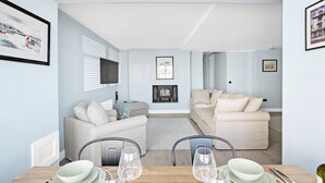 Ein modernes Wohnzimmer mit Kamin, einem Essbereich mit Tisch für zwei Personen und einer gemütlichen Sitzecke mit Sofa und Sesseln.