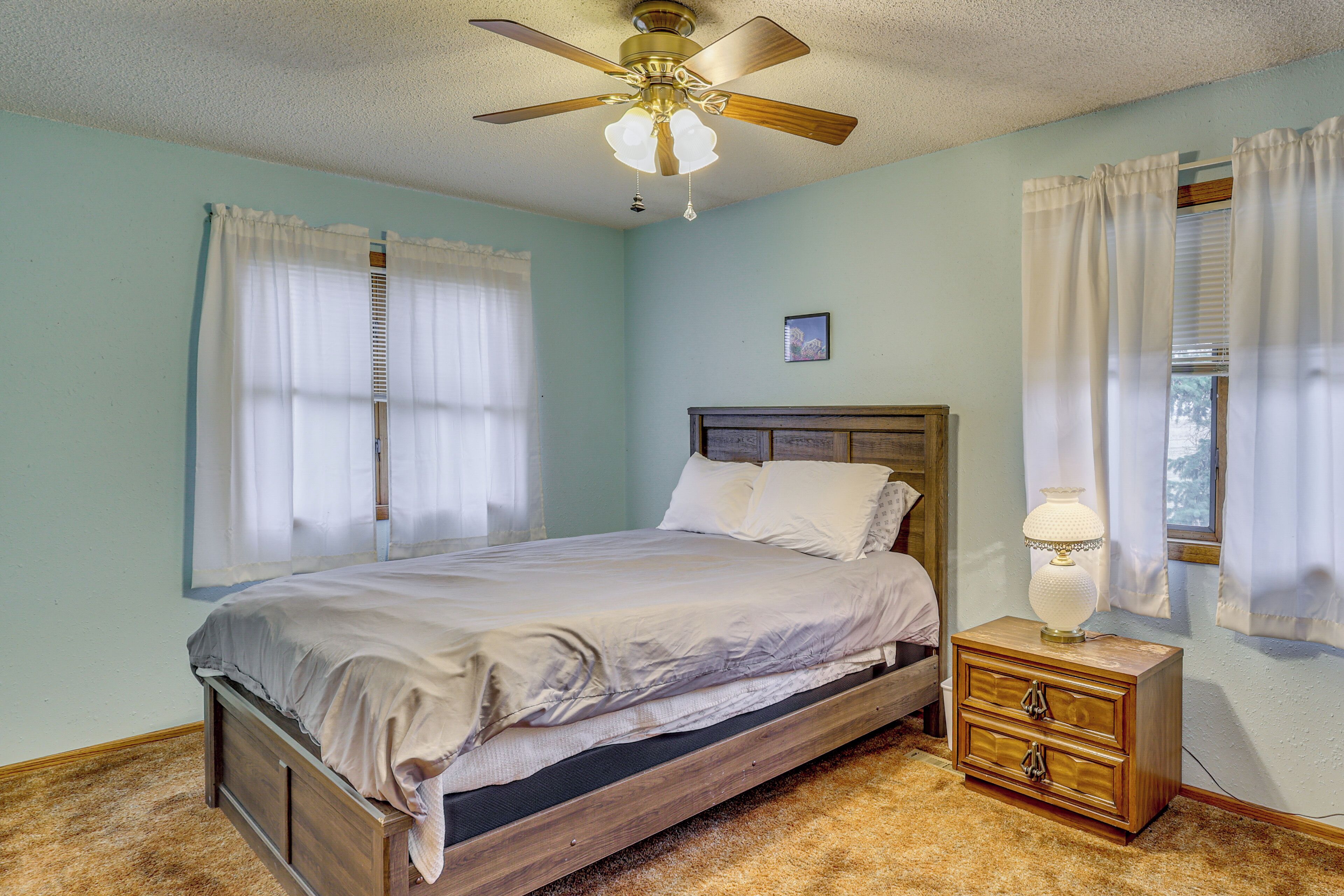 A bedroom with a bed, a nightstand, a ceiling fan, and a window with curtains.
