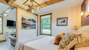 Ein Schlafzimmer mit einem großen Bett, einer Holzbalkendecke, einem Gemälde, einem Fenster und einem Schreibtisch mit Stuhl.