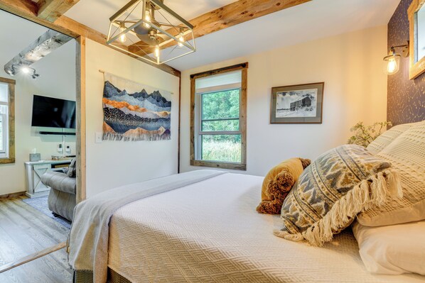 A bedroom with a large bed, a wooden ceiling, a painting, a window, and a desk with a chair. - Historic Charm + Modern Luxury: 6 Mi to Stowe Mtn (Stowe)