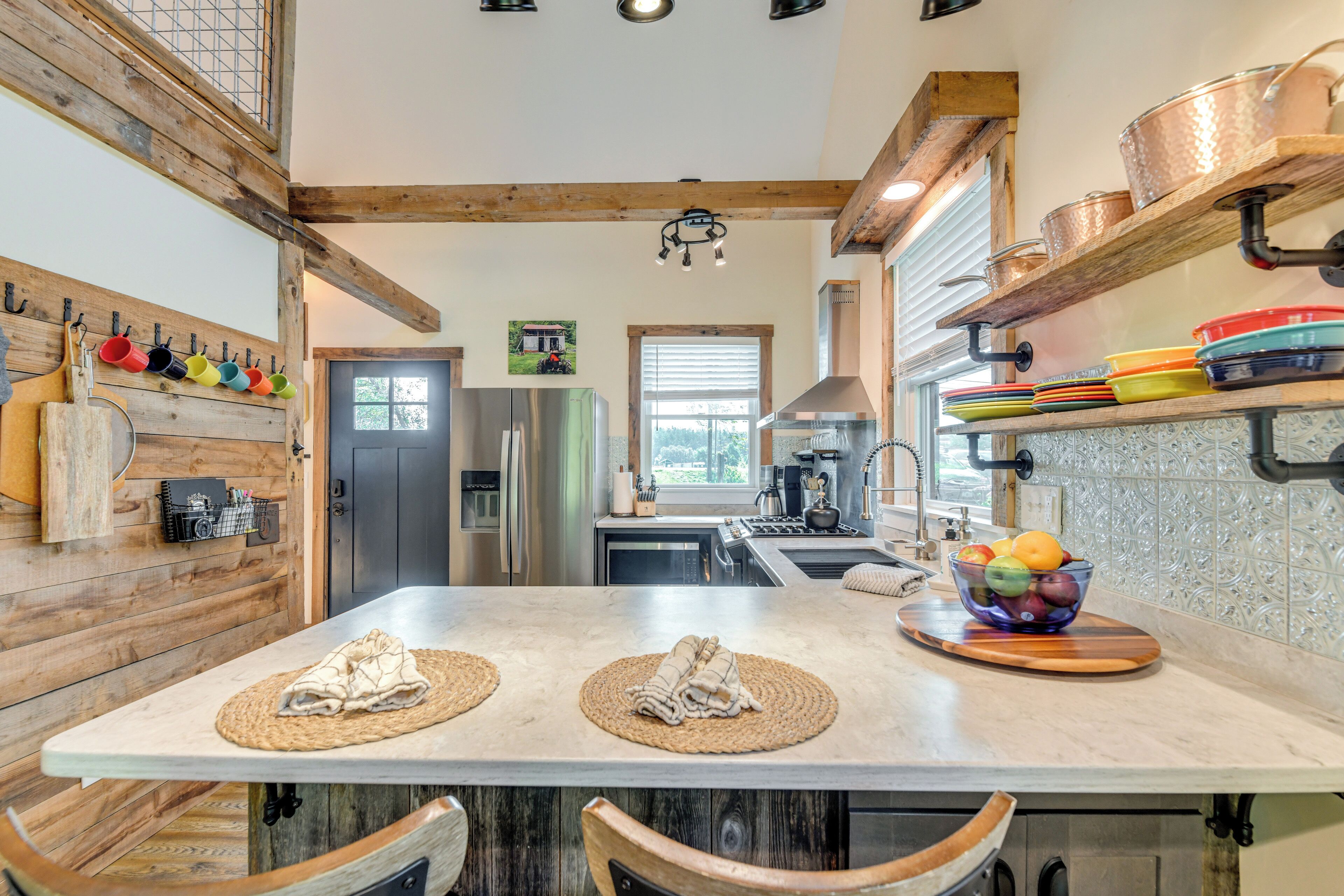 A modern kitchen with wooden beams, a central island with placemats, a fruit bowl, and stainless steel appliances.