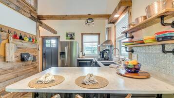 A modern kitchen with wooden beams, a central island with placemats, a fruit bowl, and stainless steel appliances.