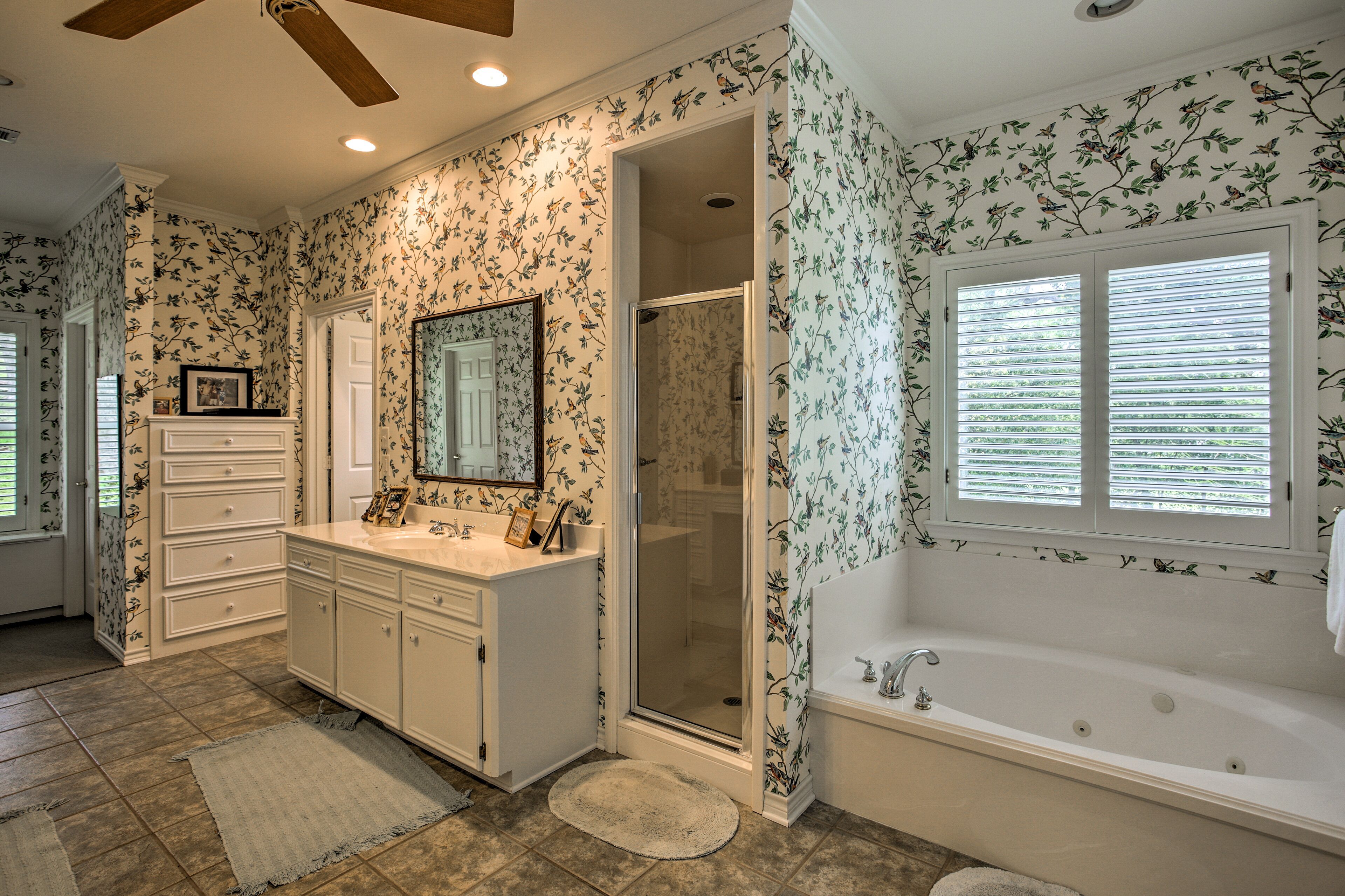 A bathroom with a vanity, a bathtub, a shower, and a window with blinds.