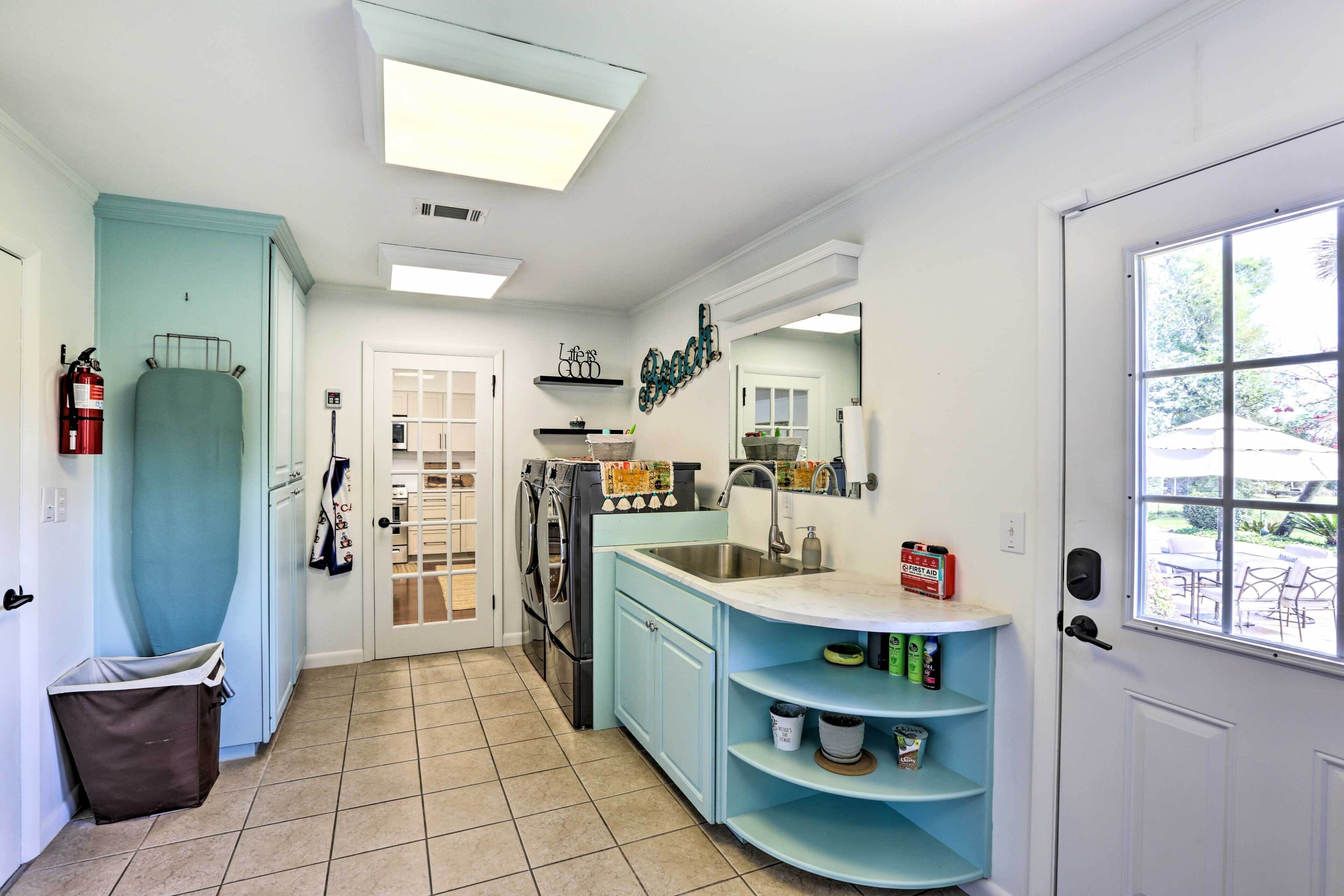 A compact kitchen with a washing machine, a sink, and a window with a view of the outdoors.