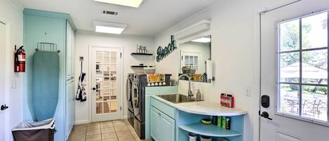 A compact kitchen with a washing machine, a sink, and a window with a view of the outdoors.