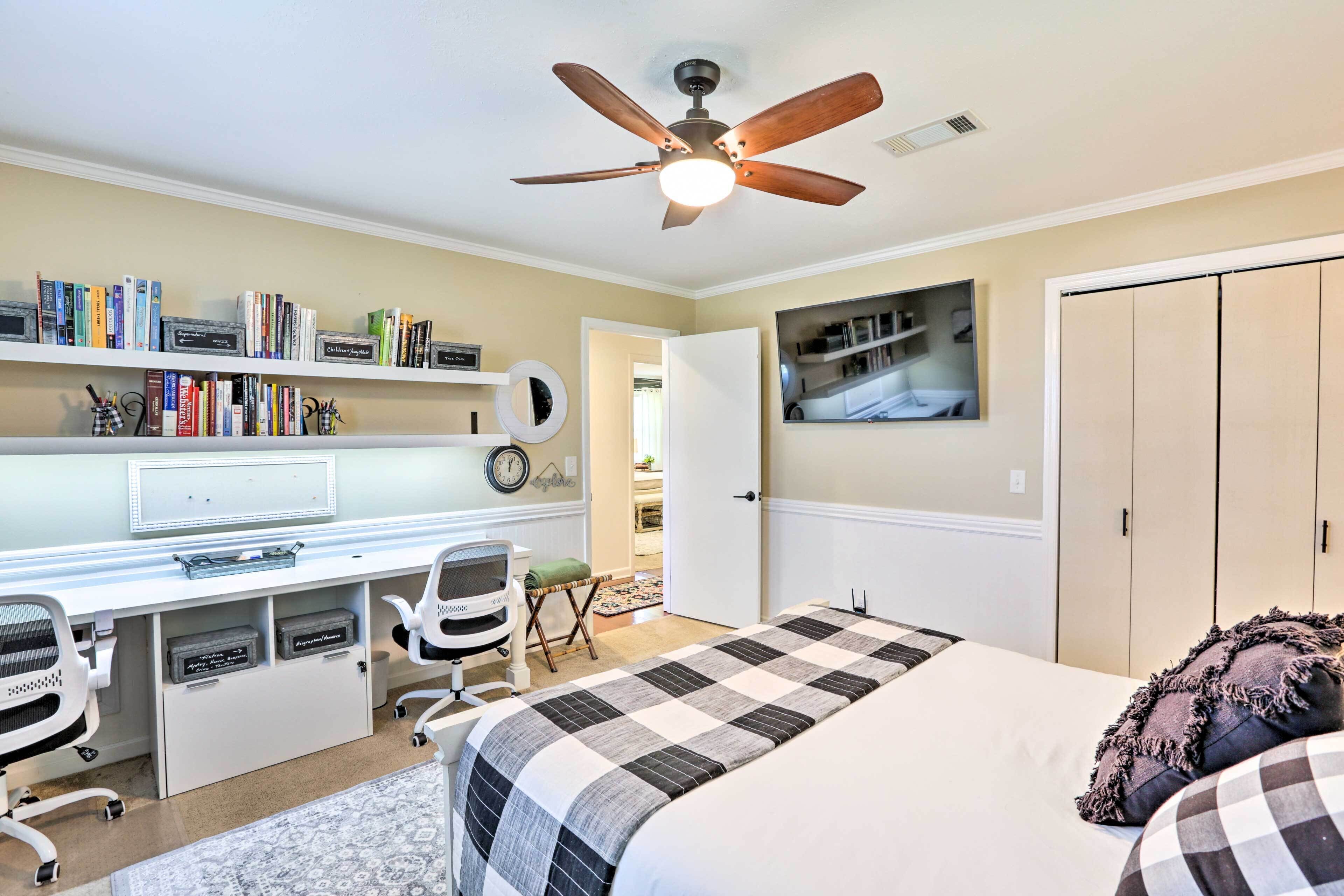 A bedroom with a bed, a desk, and a ceiling fan. There are books on shelves and a clock on the wall.