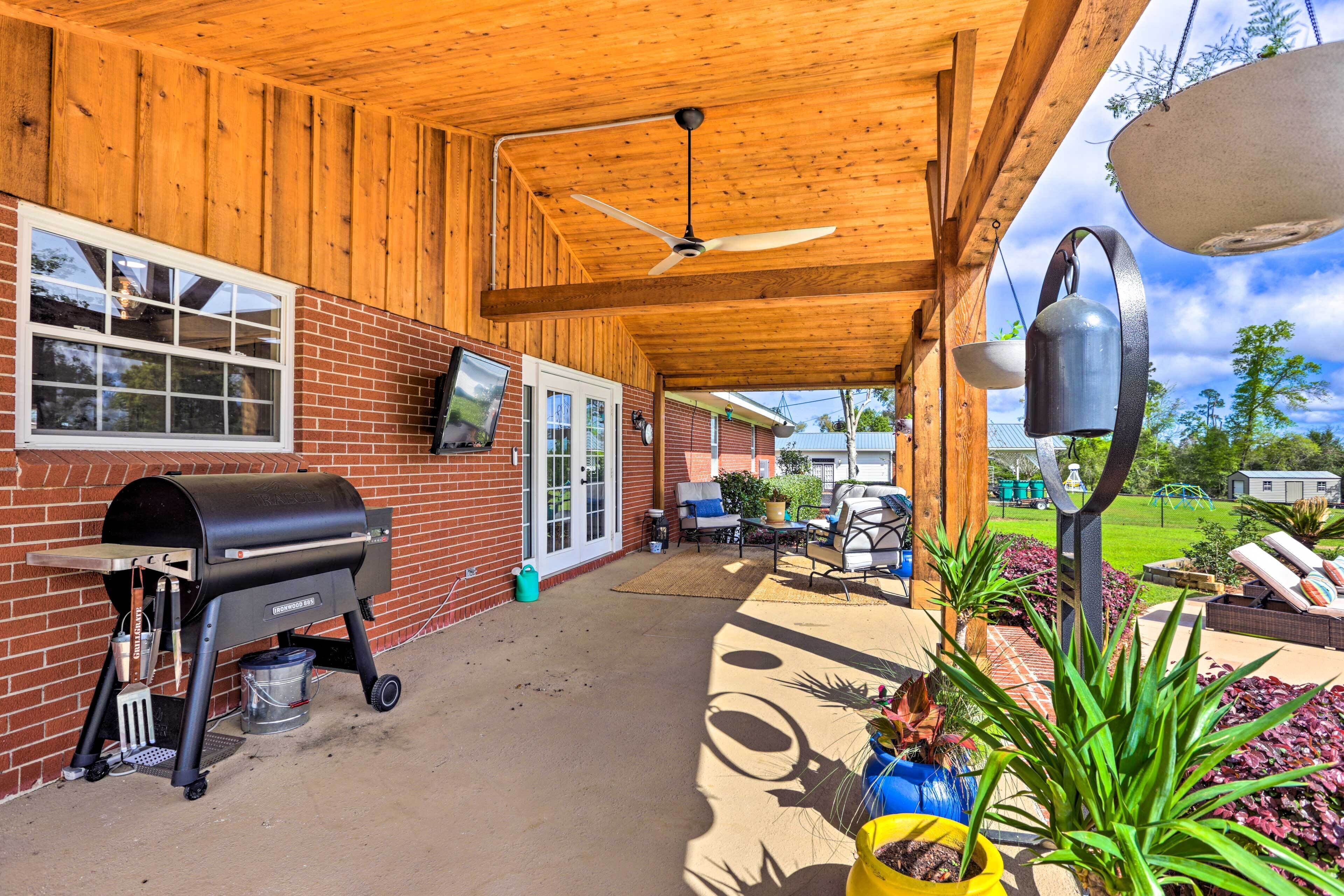 A covered patio with a barbecue grill, outdoor furniture, and potted plants.