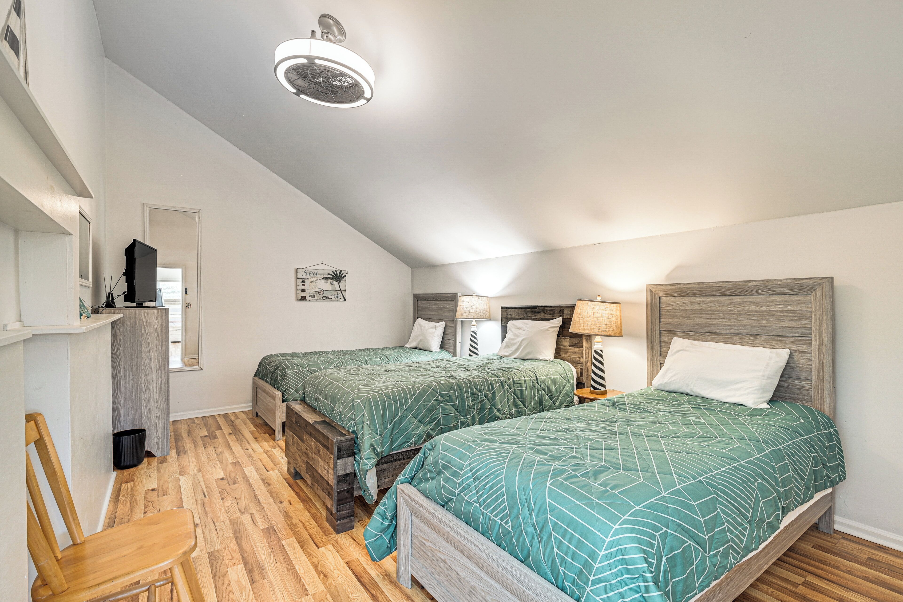A bedroom with two beds, a wooden floor, a ceiling fan, and a nightstand with a lamp.