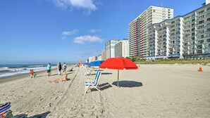 Una spiaggia con file di sedie a sdraio e ombrelloni, una riva sabbiosa e alti edifici sullo sfondo.