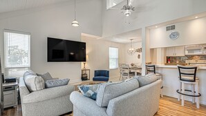 Un soggiorno moderno con un divano grigio, una TV a schermo piatto e un'area pranzo con cucina sullo sfondo.