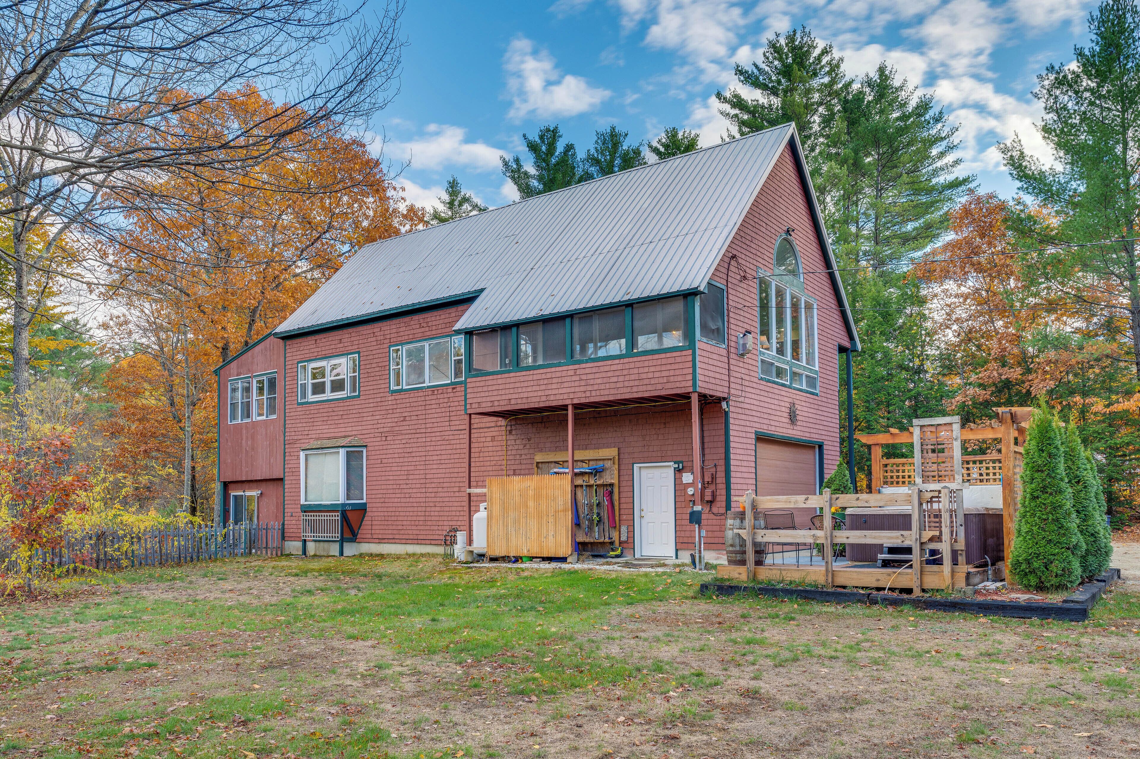 A two-story red brick house with a sloped metal roof, a front porch, and a fenced yard.