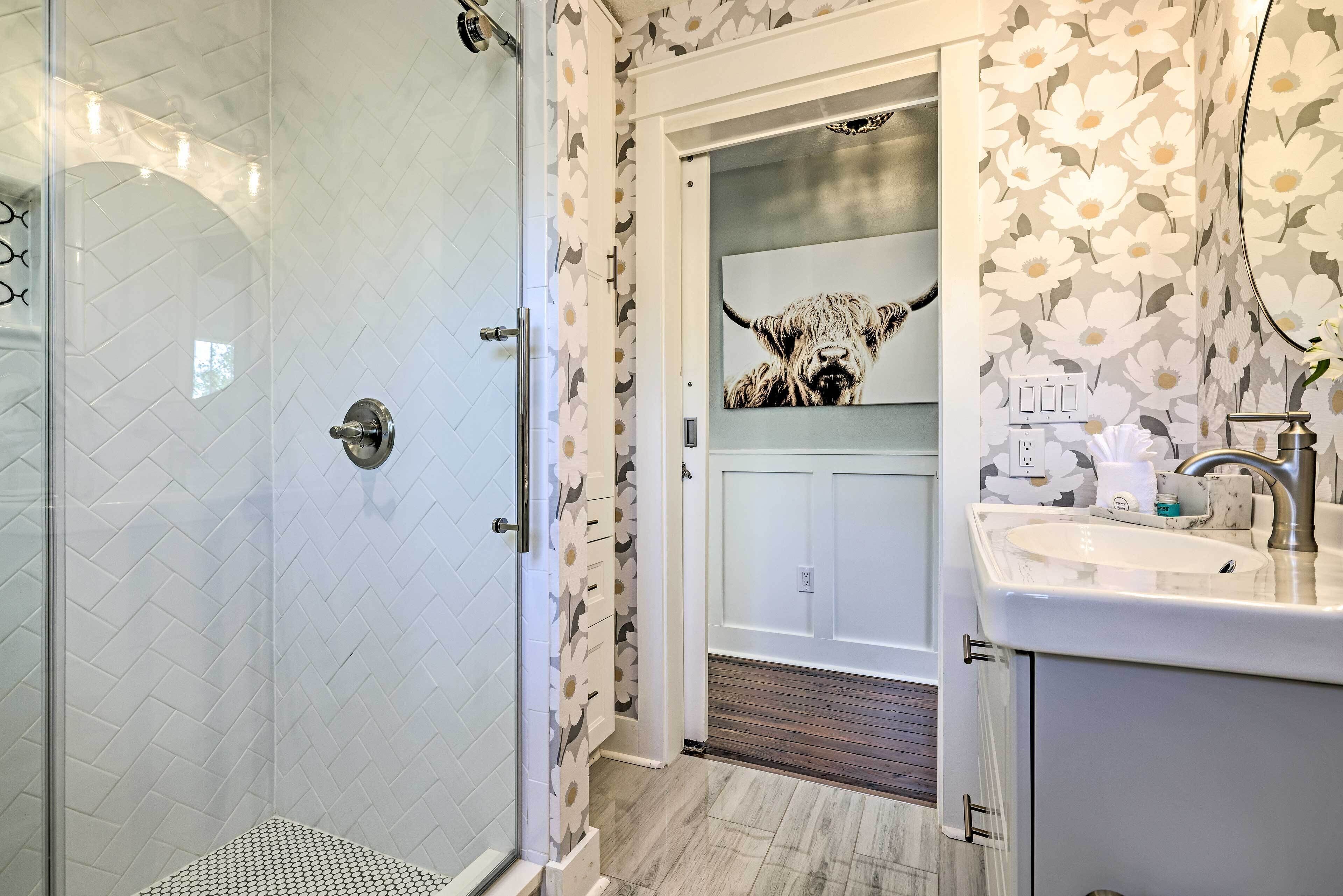 Une salle de bain avec une douche, un lavabo et une porte donnant sur une autre pièce.