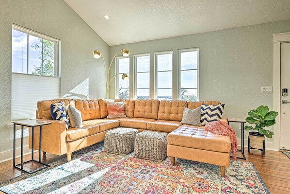 A spacious living room with a large sectional sofa, multiple windows, and a decorative rug. - Comfy Hill Country Haven w/ Private Hot Tub! (Fredericksburg)