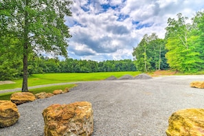 A gravel area with large rocks, a grassy field, and trees in the background.