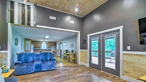 A spacious living area with a blue sofa, wooden flooring, and a kitchen in the background. - Secluded Brownsville Cabin w/ Deck & Fire Pit (Roundhill)
