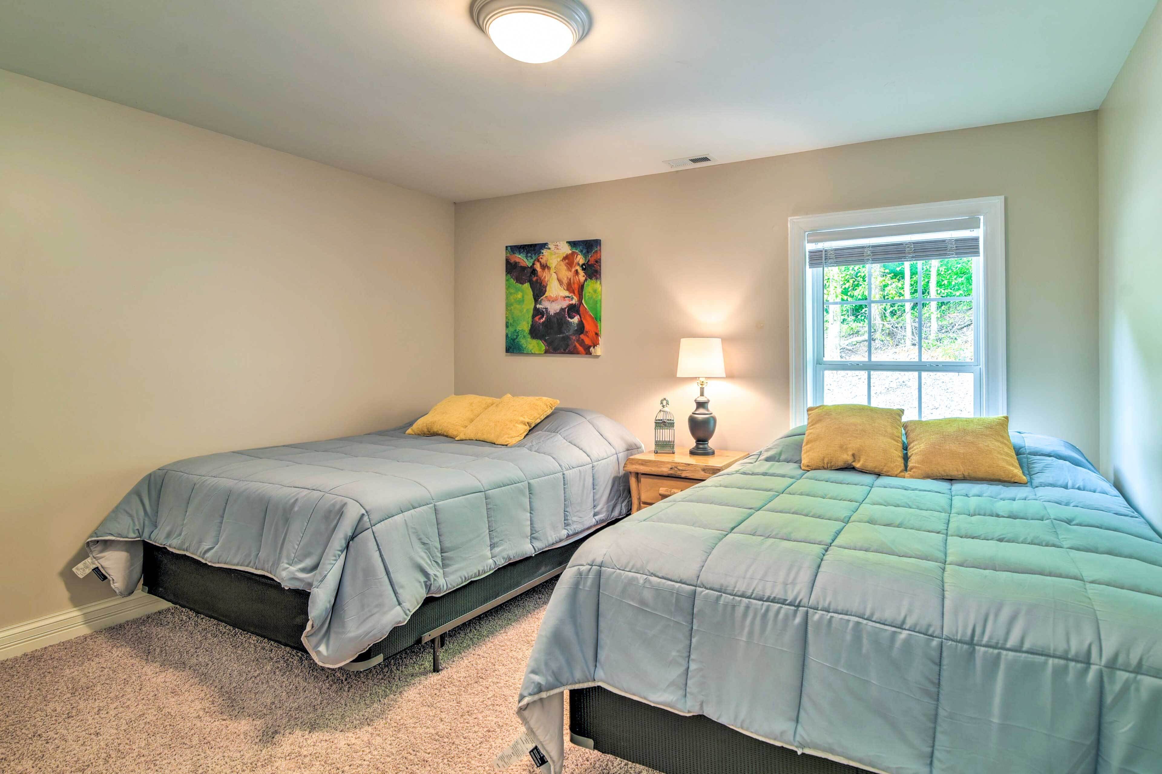 A bedroom with two beds, a nightstand, a lamp, a window with blinds, and a painting on the wall.