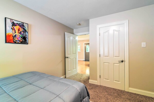 A bedroom with a bed, a door leading to another room, and a painting on the wall.