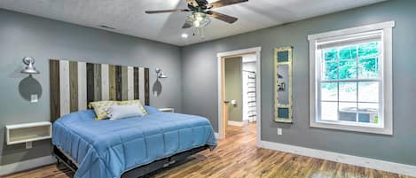 A bedroom with a bed, ceiling fan, and a large window.