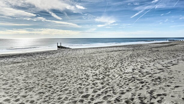 Une plage parsemée d’empreintes, une jetée et un ciel dégagé.