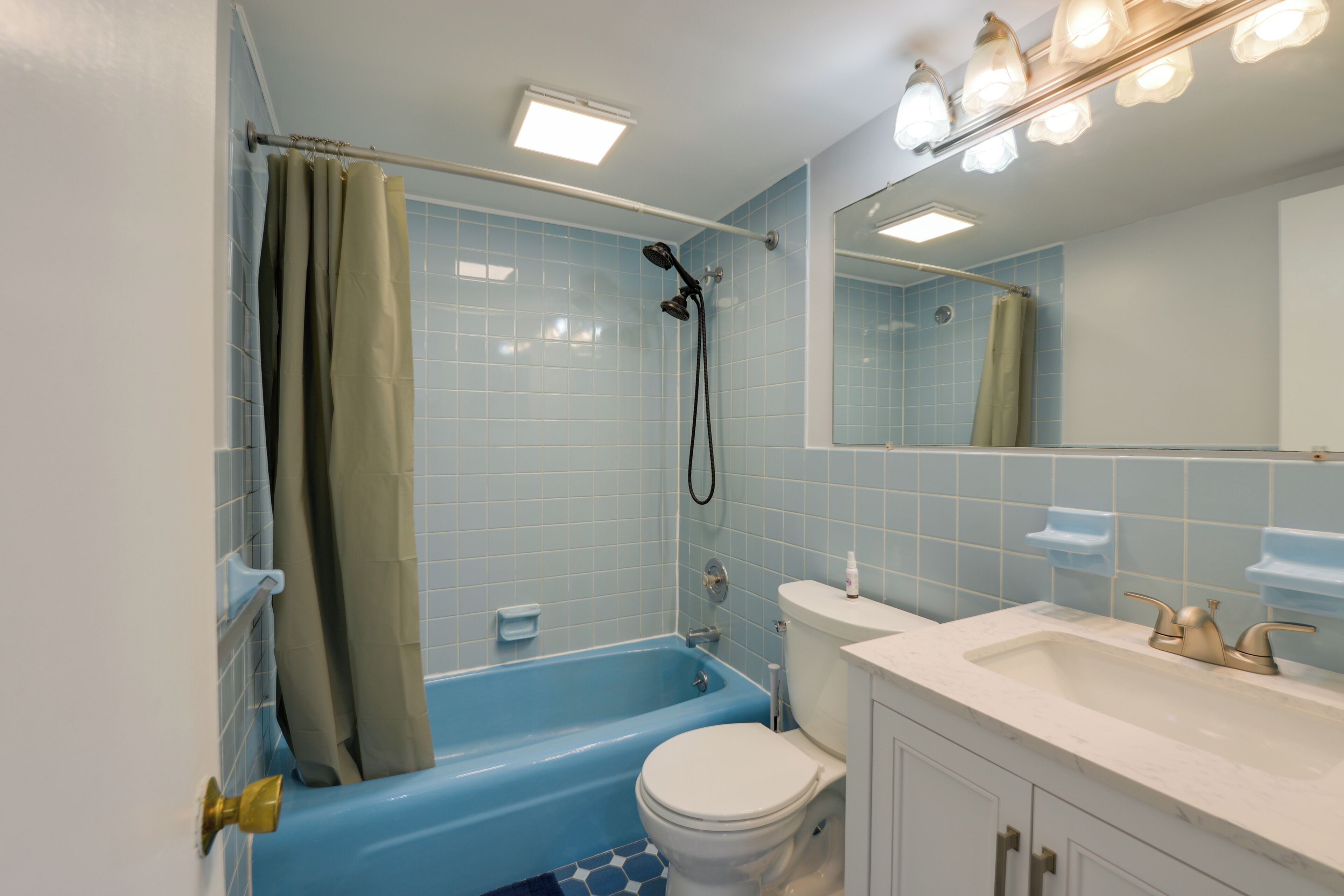 Un baño con ducha de azulejos azules, inodoro blanco y lavabo con espejo superior.