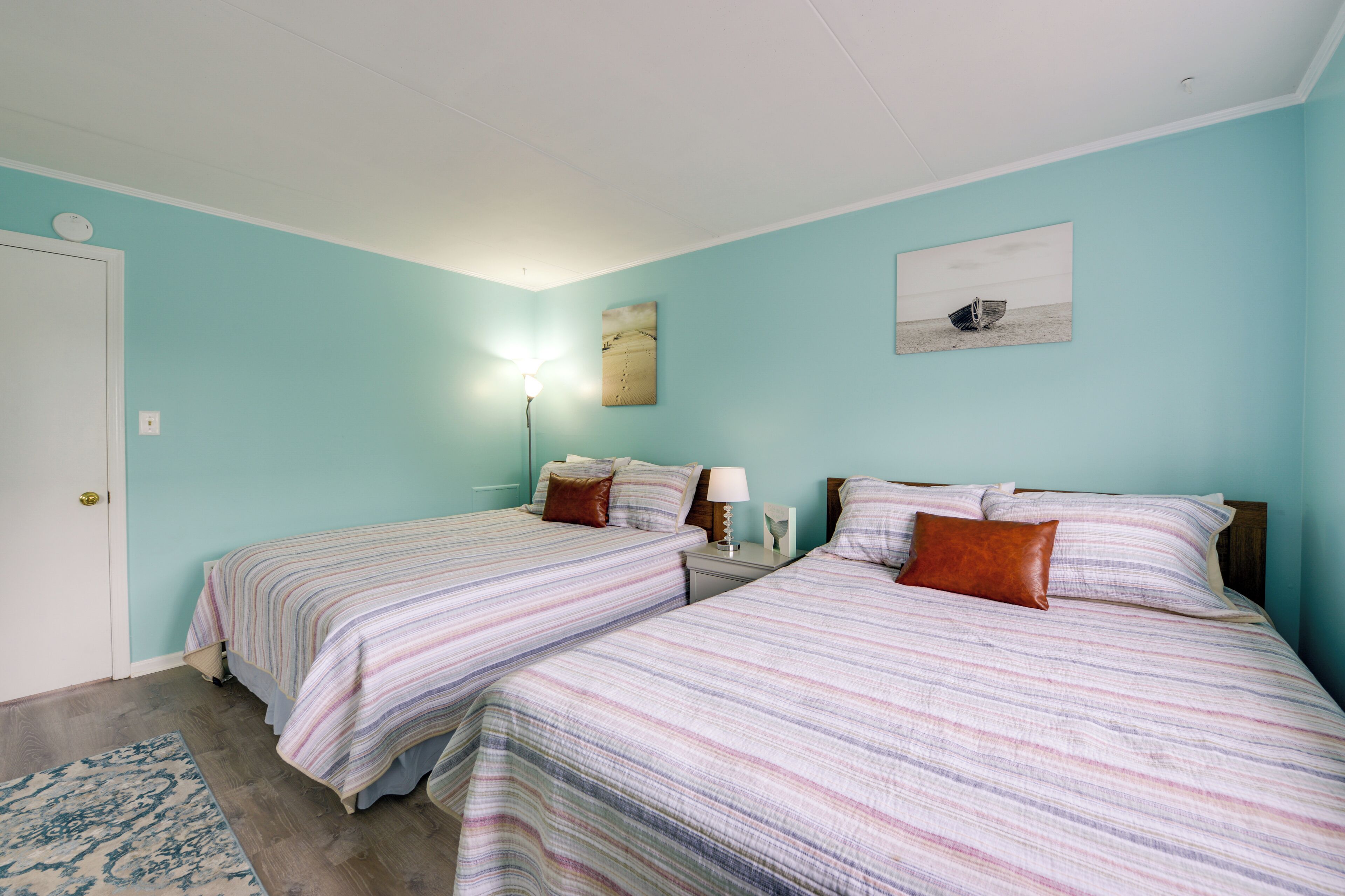 Ein Schlafzimmer mit zwei Einzelbetten, einem Nachttisch mit Lampe, einem Bild an der Wand und einer Tür mit Lichtschalter.