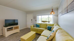 Un salon comprenant un téléviseur, un canapé jaune, un canapé beige et un meuble de rangement en bois.