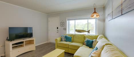 A living room with a television, a yellow sofa, a beige sofa, and a wooden entertainment unit.